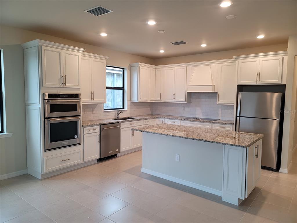 A kitchen features white cabinets, granite countertops, stainless steel appliances, and a central island — 2530 BUCKTHORN LOOP, NORTH PORT, FL