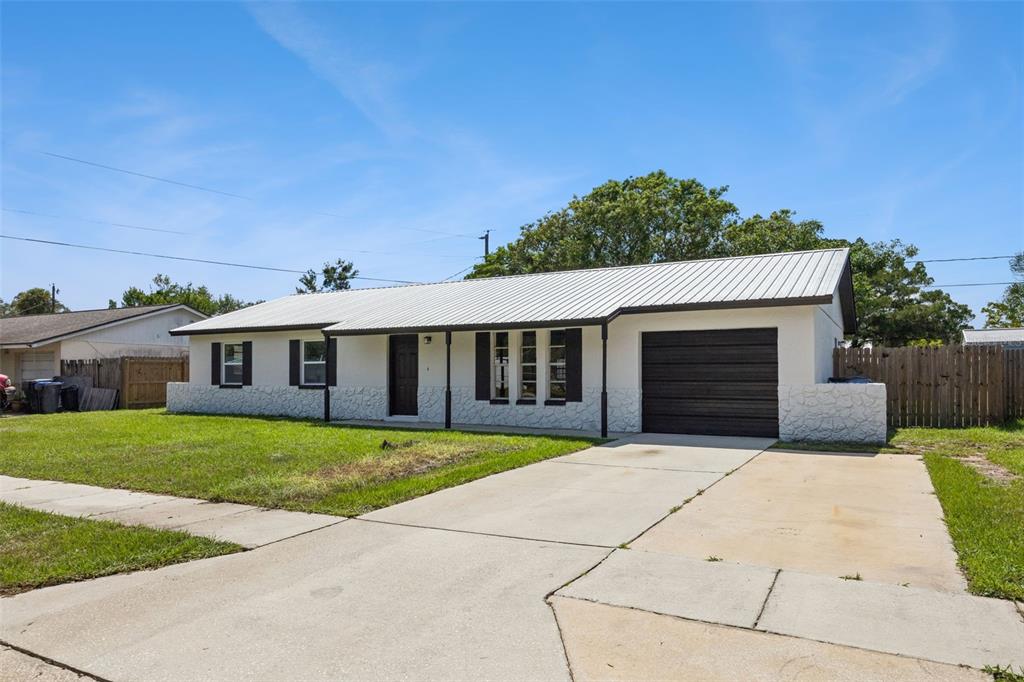 A single-story house with a white stone facade, metal roof, and attached garage — 1660 ASHWOOD AVENUE, TITUSVILLE, FL