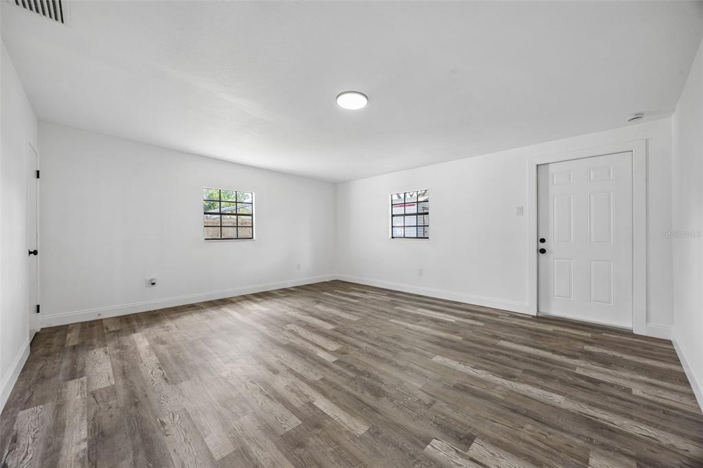 An empty room with white walls, gray wood-look flooring, two windows, and a white door — 1660 ASHWOOD AVENUE, TITUSVILLE, FL