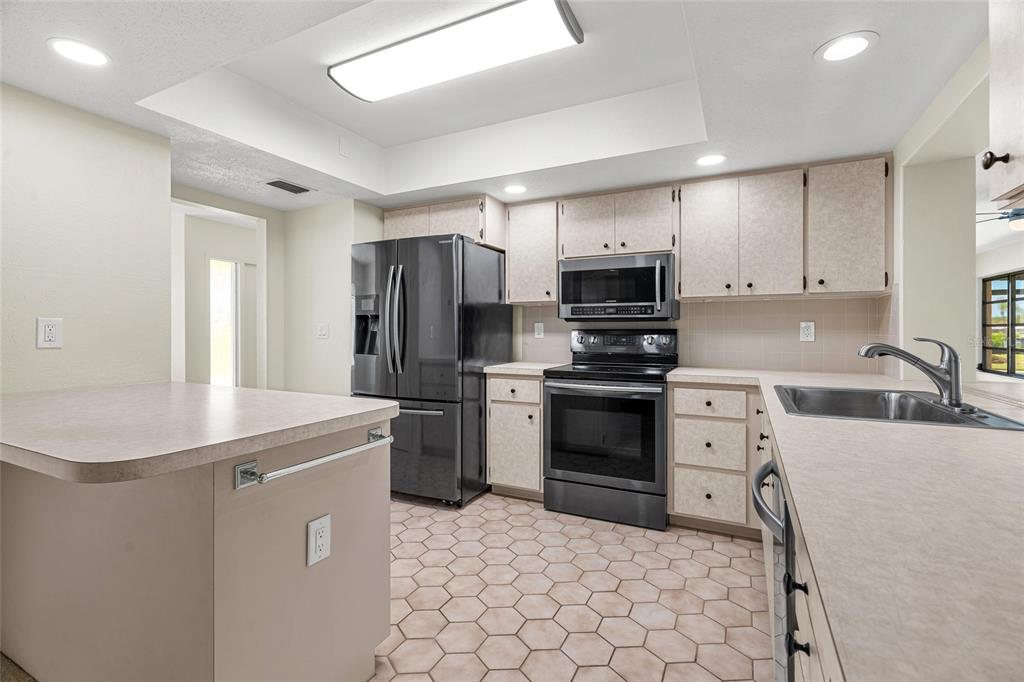 A kitchen features a black refrigerator, matching stove, light-colored cabinets, laminate countertops, and hexagonal floor tiles — 1123 MISTI COURT, VENICE, FL