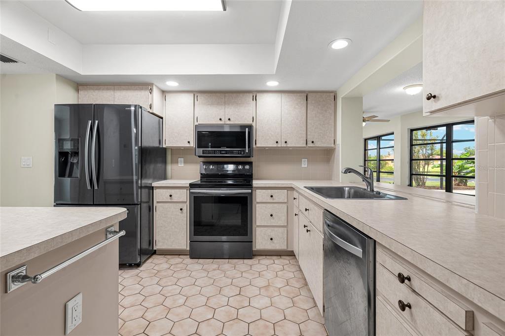A kitchen features light-colored cabinets, laminate countertops, black appliances, and hexagonal floor tiles — 1123 MISTI COURT, VENICE, FL