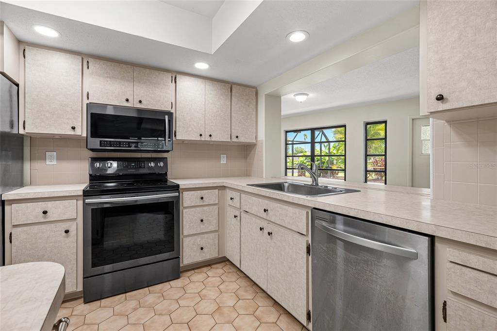 A kitchen with light-colored cabinets, stainless steel appliances, a tile floor, and a pass-through window — 1123 MISTI COURT, VENICE, FL