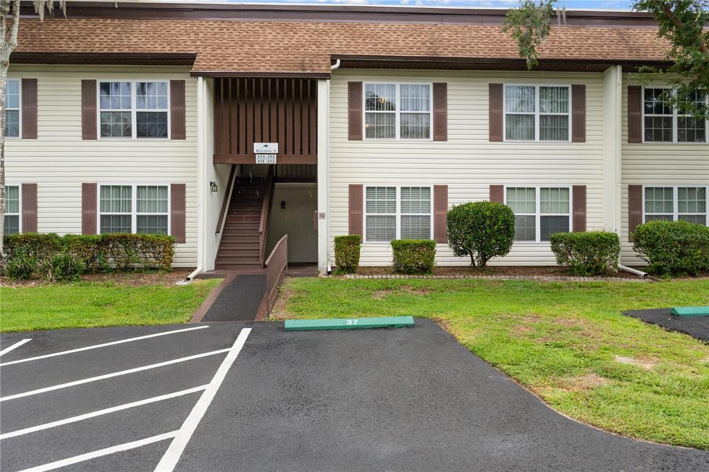 A two-story apartment building features light siding, brown shutters, and a central outdoor staircase — 2400 FOREST DRIVE UNIT 252, INVERNESS, FL