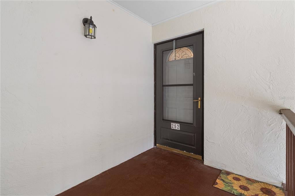 A brown front door with a glass storm door sits on a covered porch — 2400 FOREST DRIVE UNIT 252, INVERNESS, FL