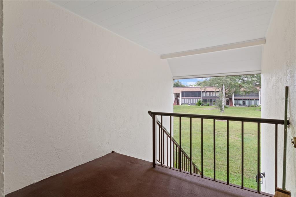 An outdoor balcony with a brown floor, white walls, and a metal railing overlooking grass — 2400 FOREST DRIVE UNIT 252, INVERNESS, FL