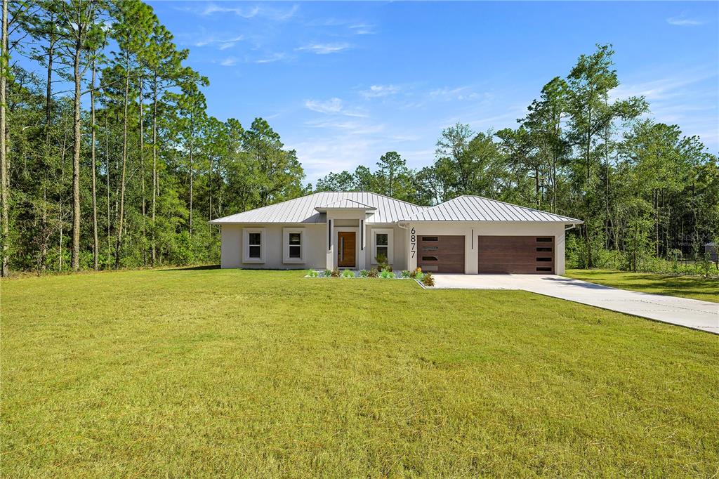 A modern single-story house with a metal roof and two-car garage sits on a grassy lot — 6877 SW 131ST CIRCLE, OCALA, FL