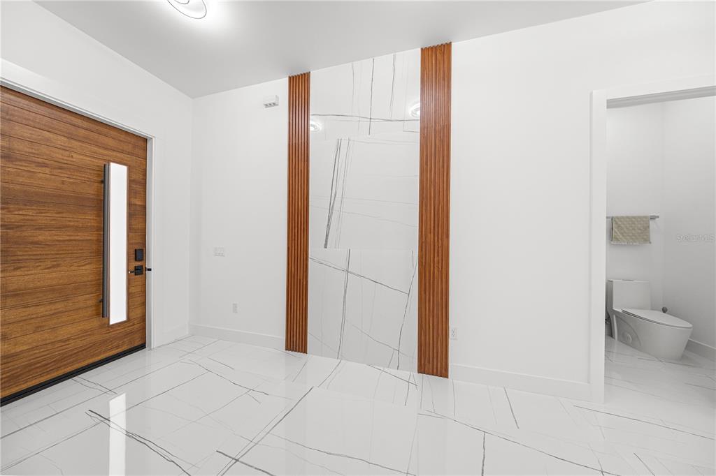 An entryway features a wood door, white marble-look tile floors, and a vertical wood-accented wall — 6877 SW 131ST CIRCLE, OCALA, FL