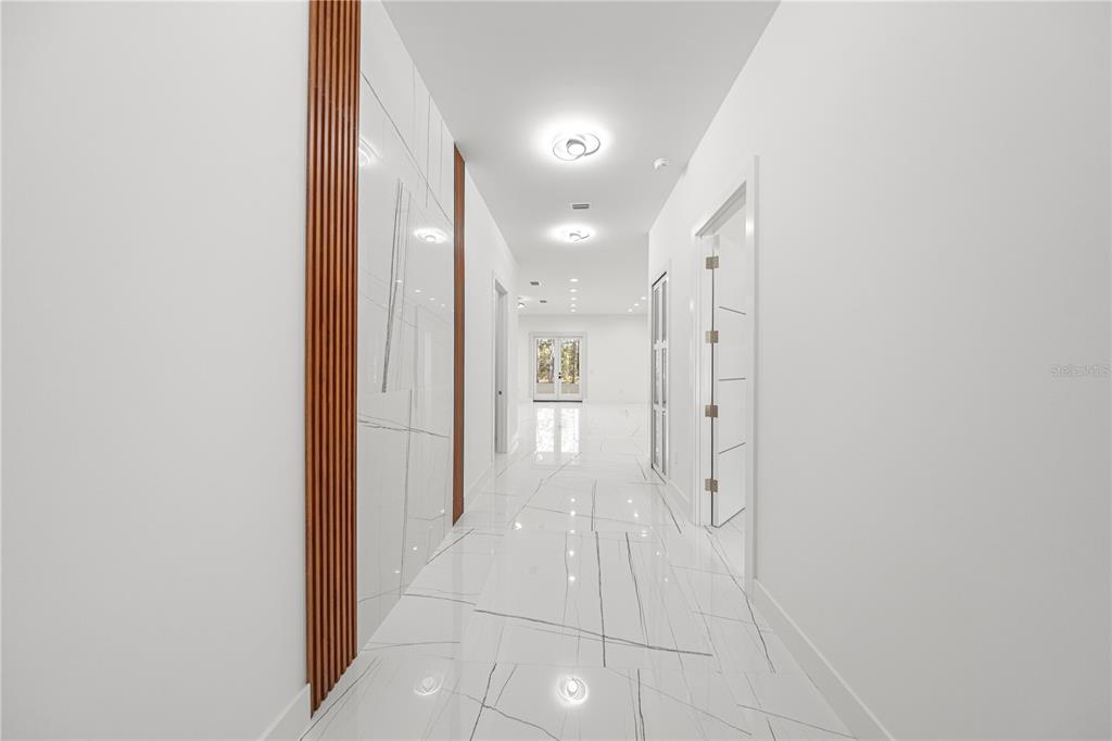 A bright hallway features white marble floors, a wood-slatted accent wall, and recessed lighting — 6877 SW 131ST CIRCLE, OCALA, FL