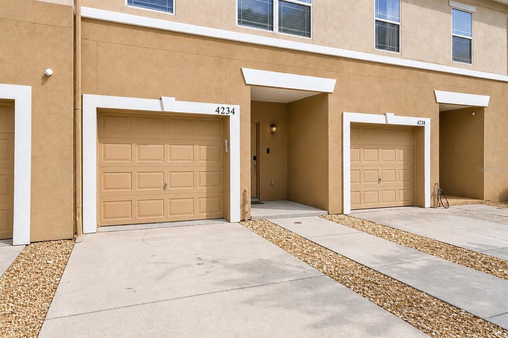 The exterior of a tan townhouse features two garage doors and a recessed entryway — 4234 TYLER CIRCLE N UNIT #102B, ST PETERSBURG, FL