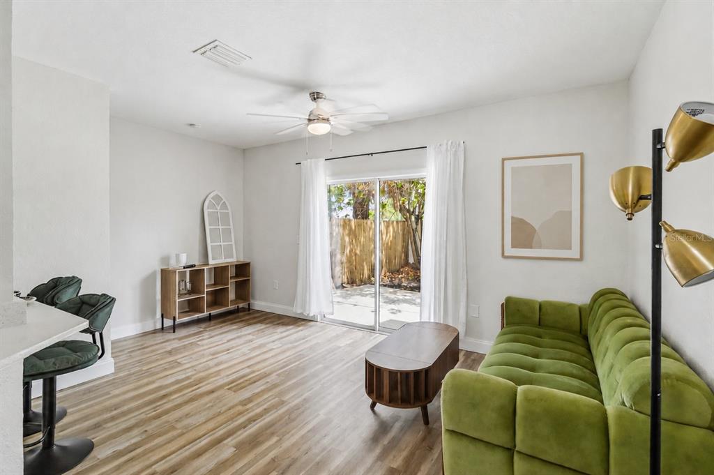 A living room features a green tufted sofa, wood-look flooring, and sliding glass patio doors — 4234 TYLER CIRCLE N UNIT #102B, ST PETERSBURG, FL