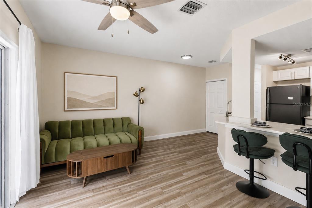 A living room with a green sofa, wood coffee table, and an adjacent kitchen counter — 4234 TYLER CIRCLE N UNIT #102B, ST PETERSBURG, FL