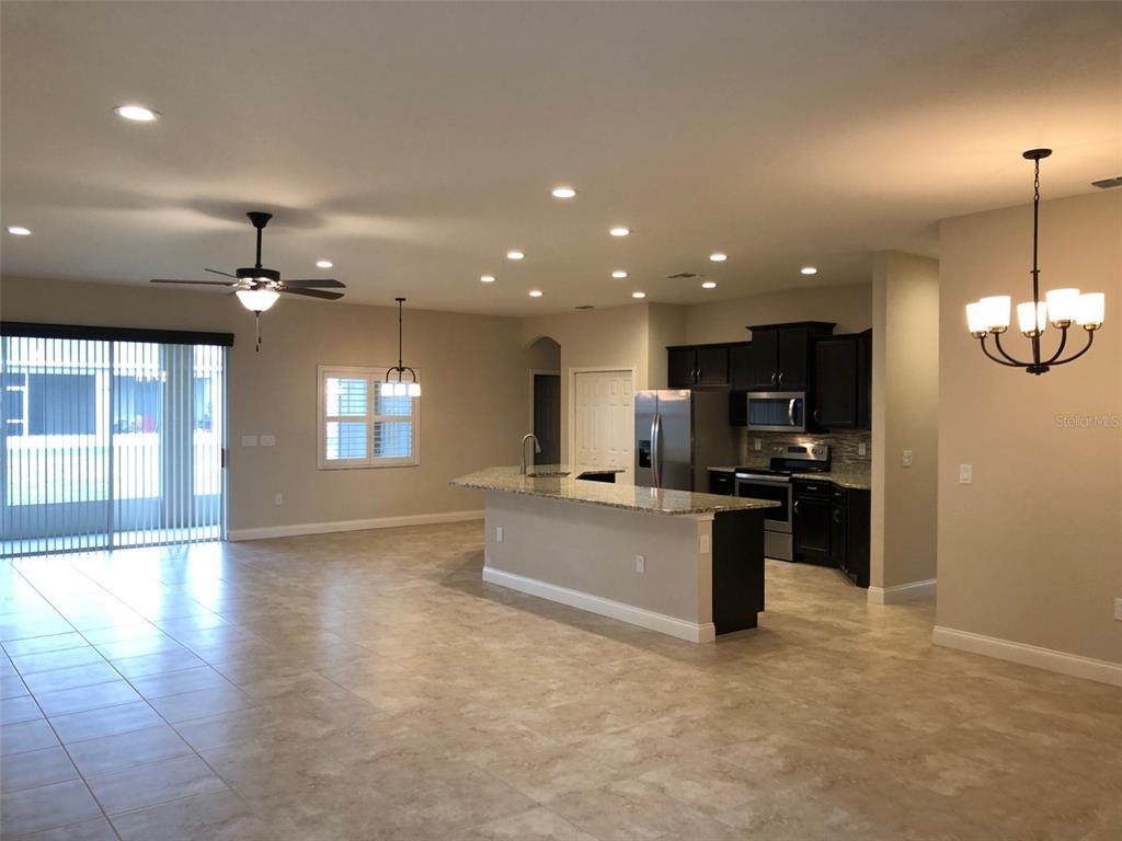 An open-concept kitchen features dark cabinetry, granite countertops, and a large island — 6063 HIGHLANDS GRACE BOULEVARD, LAKELAND, FL