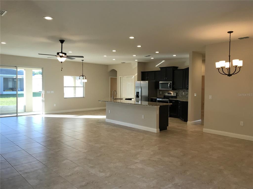 An open-concept kitchen and living area features tile flooring, dark cabinetry, and a granite island — 6063 HIGHLANDS GRACE BOULEVARD, LAKELAND, FL