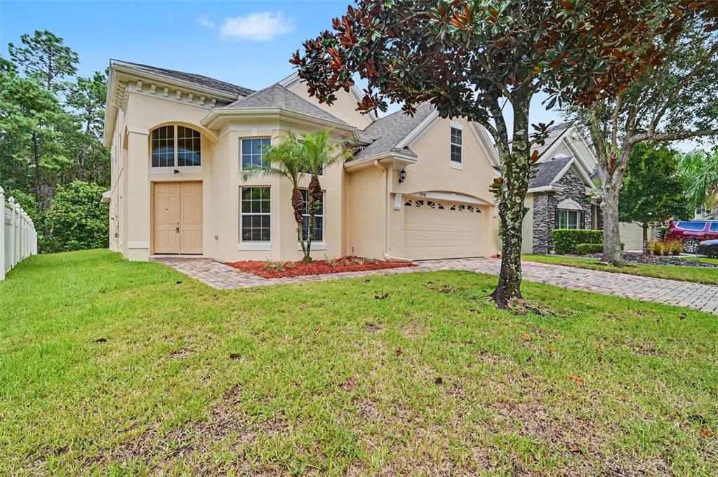 A two-story beige stucco house with a paved driveway, a two-car garage, and landscaping — 10546 WILLOW RIDGE LOOP, ORLANDO, FL