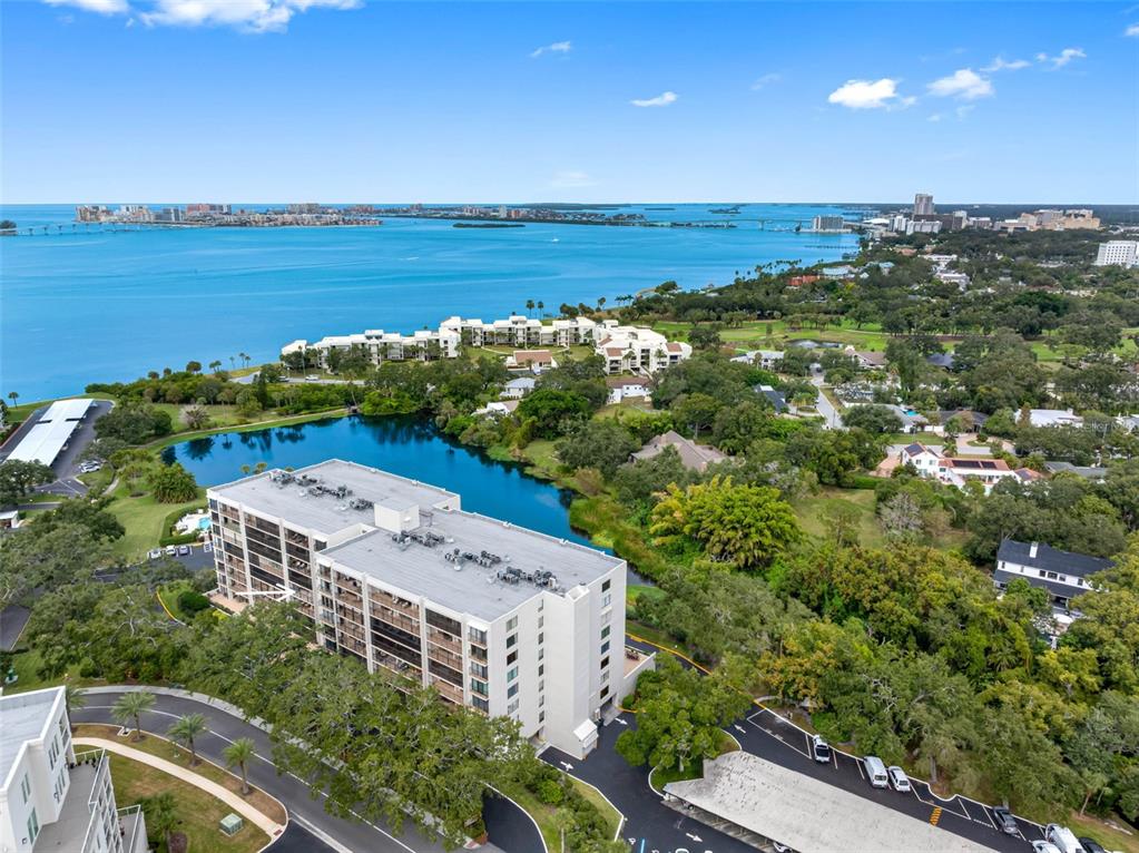 An aerial view shows a multi-story apartment building situated next to a lake and bay — 220 BELLEVIEW BOULEVARD UNIT 412, BELLEAIR, FL