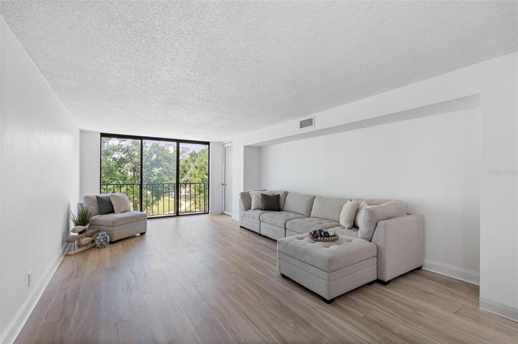 A living room features light wood-look flooring, a sectional sofa, an armchair, and floor-to-ceiling windows — 220 BELLEVIEW BOULEVARD UNIT 412, BELLEAIR, FL