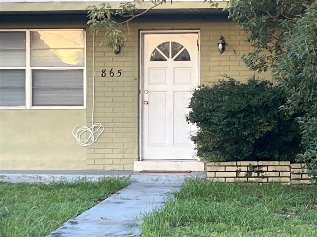 A white front door with a semi-circular window is set into a light green brick wall — 865 CANADA STREET NE, PALM BAY, FL