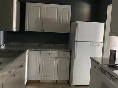 A kitchen features white cabinets, granite-look countertops, and a white refrigerator against dark walls — 865 CANADA STREET NE, PALM BAY, FL