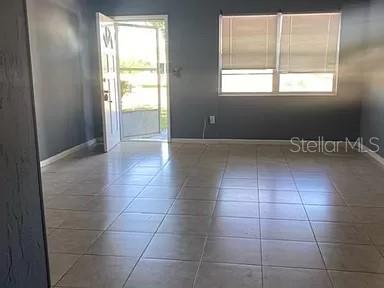 An empty room features gray walls, light-colored tile flooring, and a door leading outside — 865 CANADA STREET NE, PALM BAY, FL