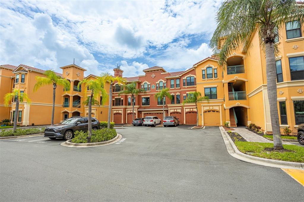 A multi-story apartment complex with orange stucco walls, palm trees, and a parking lot — 2717 VIA CIPRIANI UNIT 621B, CLEARWATER, FL