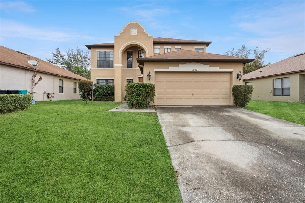 A two-story tan stucco house features a front-facing garage and a curved entryway arch — 4867 SWEET CEDAR CIRCLE, ORLANDO, FL