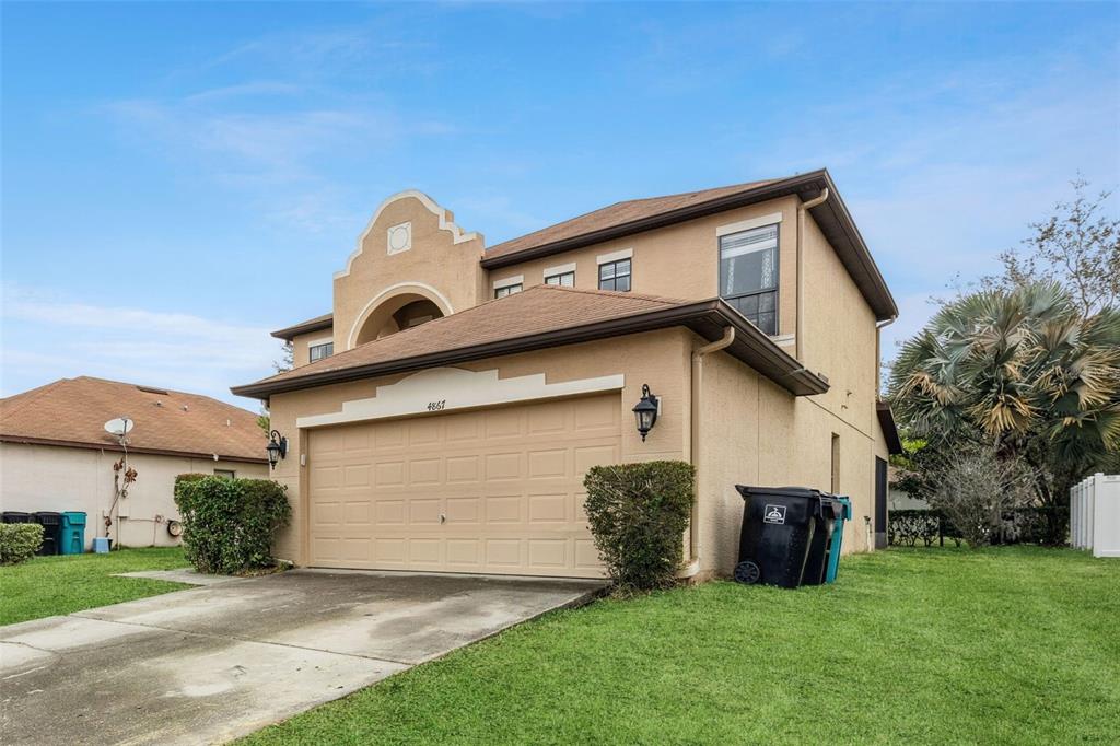 A two-story tan stucco house features a two-car garage and a decorative arched roofline — 4867 SWEET CEDAR CIRCLE, ORLANDO, FL