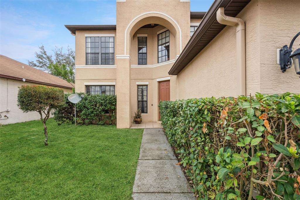 A beige two-story house features a front walkway, a small lawn, and manicured hedges — 4867 SWEET CEDAR CIRCLE, ORLANDO, FL