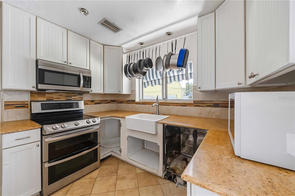 A kitchen with white cabinets, stainless steel appliances, a farmhouse sink, and tan countertops — 2507 RIVERVIEW BOULEVARD, BRADENTON, FL