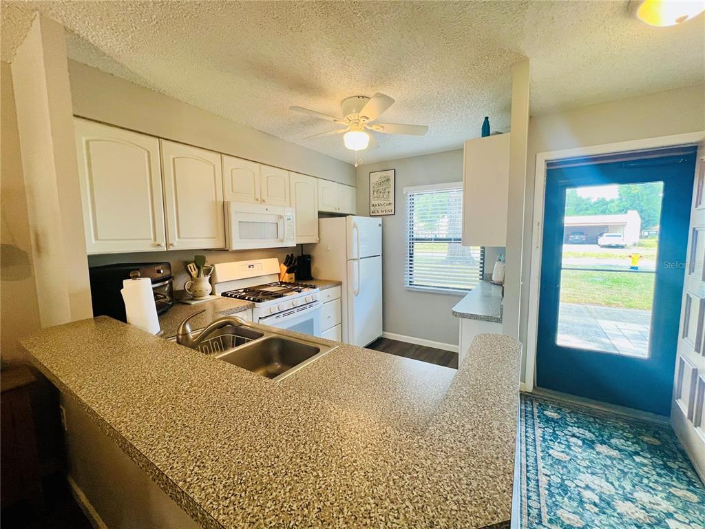 A kitchen with white cabinets, granite-look countertops, a white refrigerator, and a blue exterior door — 2955 FLINT DRIVE S, CLEARWATER, FL