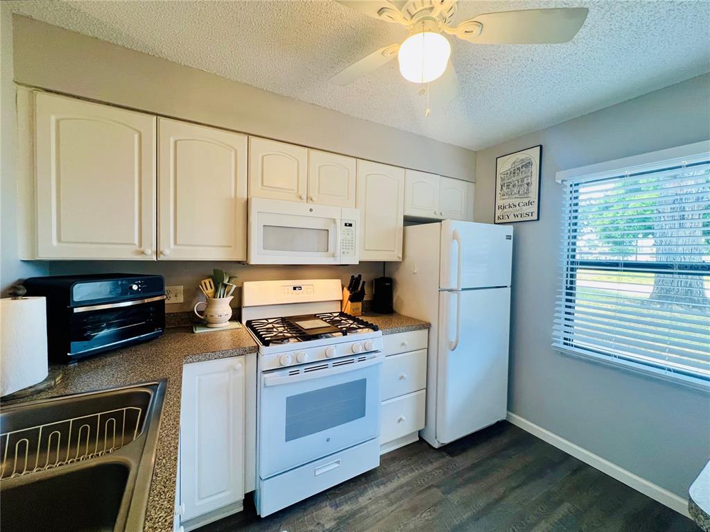 A kitchen features white cabinets, white appliances, a ceiling fan, and a window with blinds — 2955 FLINT DRIVE S, CLEARWATER, FL