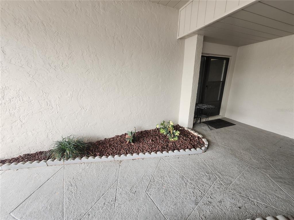 A covered patio features a textured concrete floor, a stucco wall, and a small garden bed — 1513 16TH CIRCLE SE UNIT 43, LARGO, FL