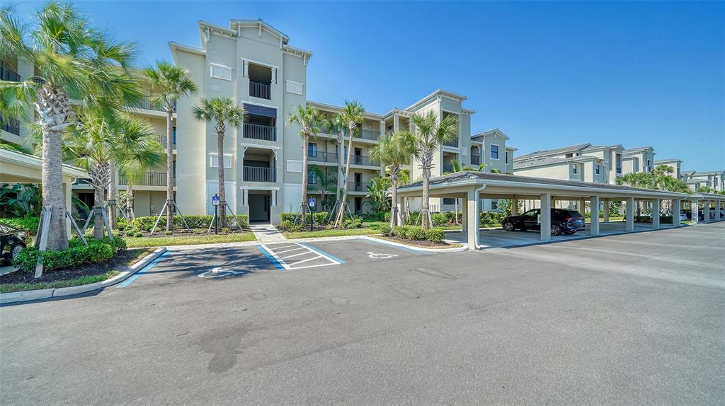 A multi-story apartment building with palm trees, a parking lot, and a covered carport — 18028 GAWTHROP DRIVE UNIT 306, BRADENTON, FL