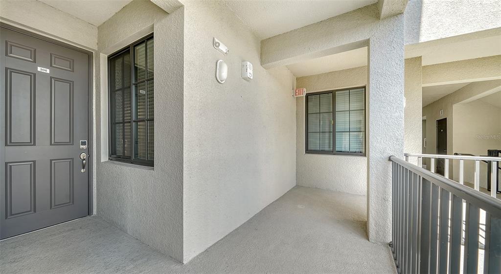 An exterior apartment hallway features a grey door, two windows, and a metal railing — 18028 GAWTHROP DRIVE UNIT 306, BRADENTON, FL