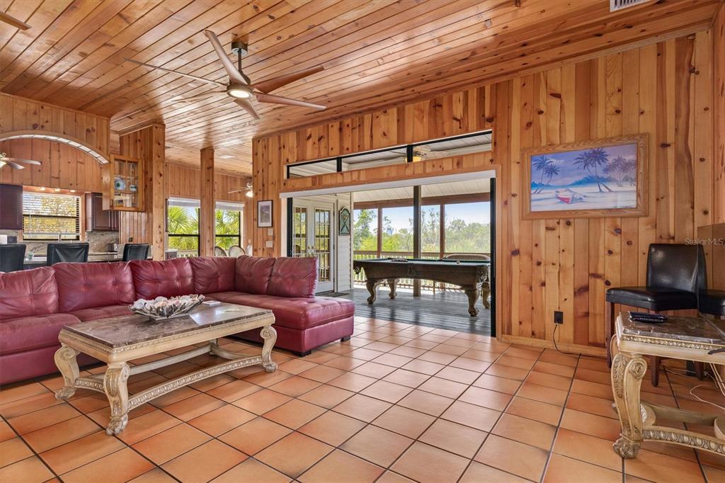 A living room with wood-paneled walls, a red sectional sofa, and a pool table outside — 51 PALM DRIVE, PLACIDA, FL