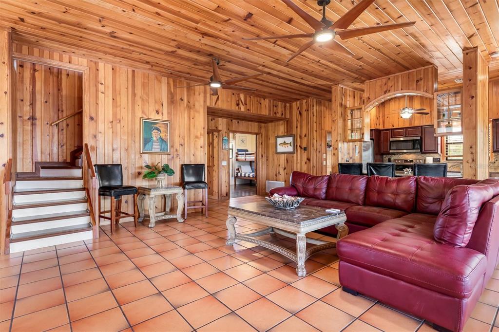 A living room with wood-paneled walls, tile flooring, a red sectional sofa, and a staircase — 51 PALM DRIVE, PLACIDA, FL
