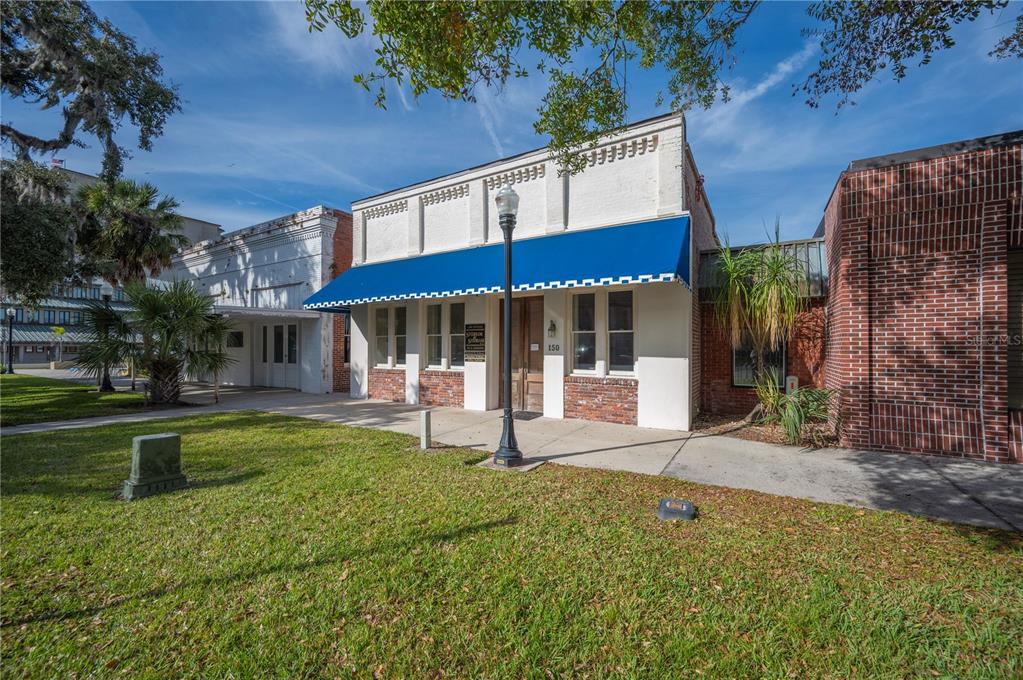 A white commercial building with a blue awning sits beside a brick building — 150 E DAVIDSON STREET, BARTOW, FL