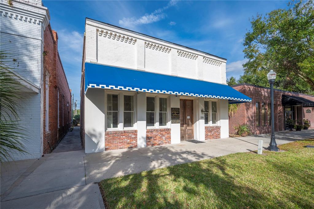 A white brick commercial building features a blue awning, large windows, and a wooden door — 150 E DAVIDSON STREET, BARTOW, FL