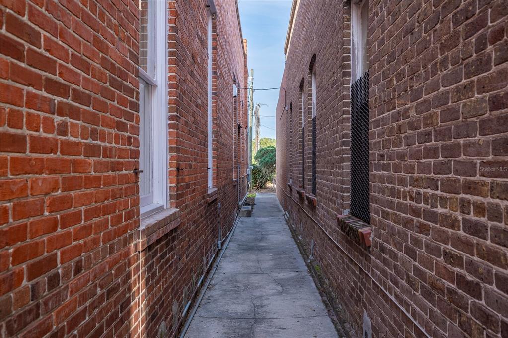 A narrow concrete alleyway sits between two historic red brick buildings with tall windows — 150 E DAVIDSON STREET, BARTOW, FL