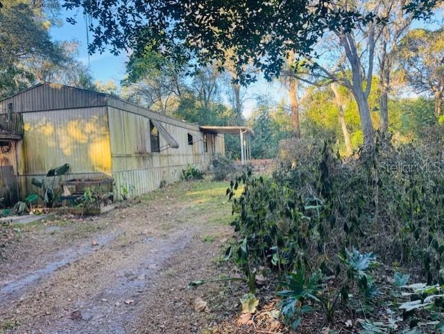 An exterior view of a weathered mobile home situated on a wooded, overgrown lot — 4547 CR 692, WEBSTER, FL