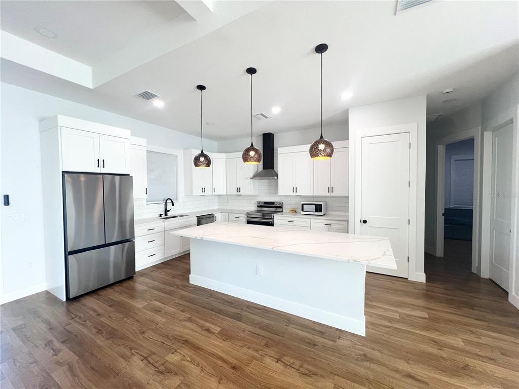 A modern kitchen features white cabinetry, stainless steel appliances, a marble-topped island, and wood flooring — 4317 MEAGER CIRCLE, PORT CHARLOTTE, FL