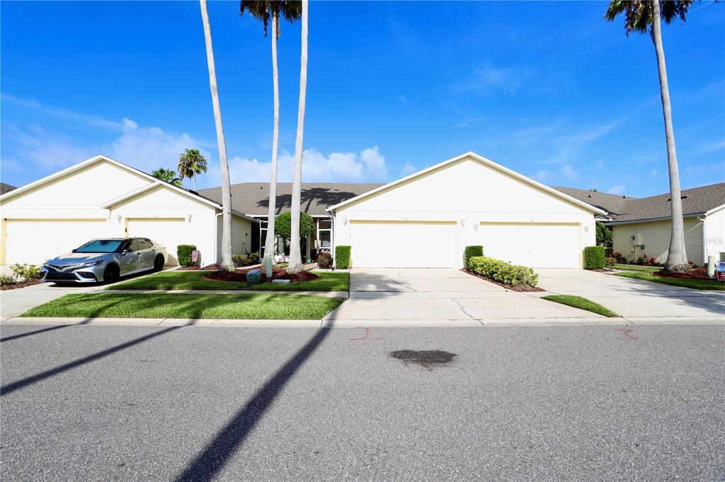 A beige single-story house with a two-car garage, palm trees, and a concrete driveway — 170 CLUB VILLAS LANE, KISSIMMEE, FL