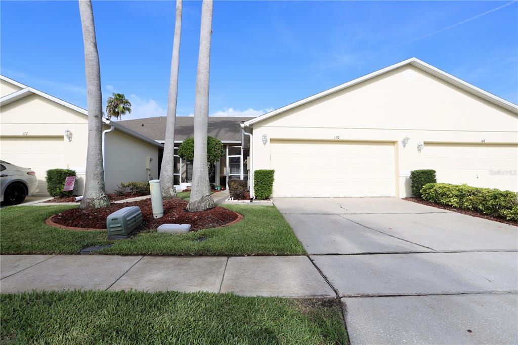 A street-level view of a light-colored duplex with two garages and palm trees — 170 CLUB VILLAS LANE, KISSIMMEE, FL