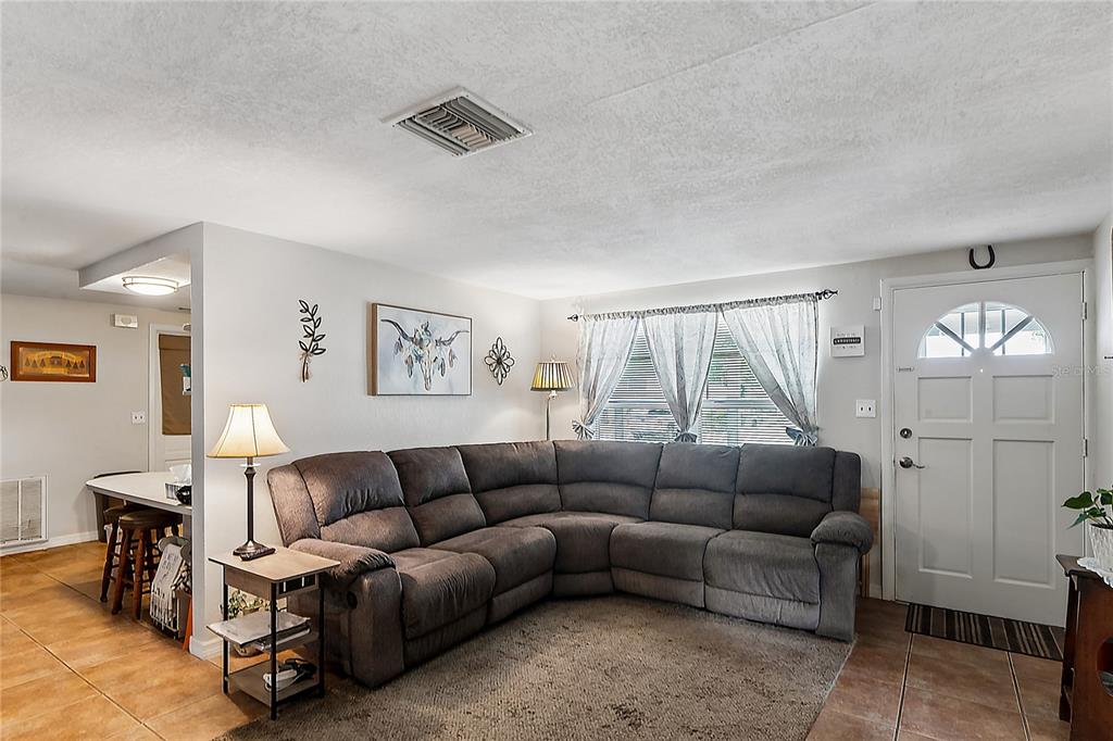 A living room features a gray sectional sofa, tile flooring, and a white front door — 7106 PALISADE DRIVE, PORT RICHEY, FL