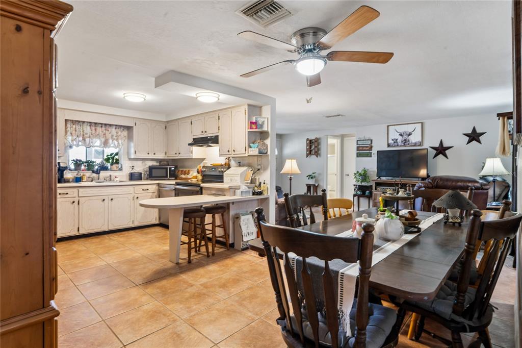 An open-concept kitchen and dining area featuring white cabinetry, tile flooring, and a ceiling fan — 7106 PALISADE DRIVE, PORT RICHEY, FL