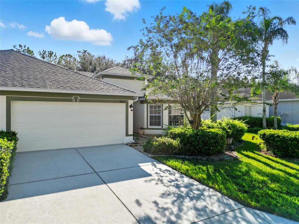 A single-story house with a white garage door, a concrete driveway, and surrounding landscaping — 9427 ROLLING CIRCLE, SAN ANTONIO, FL