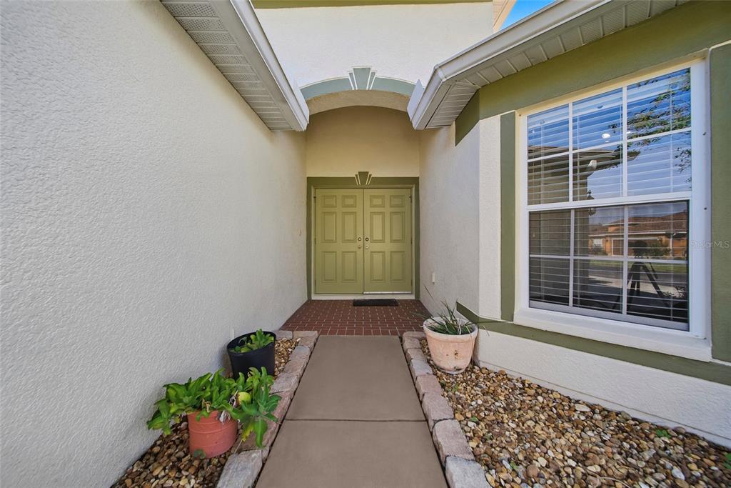 A concrete walkway leads to the double front doors of a house with stucco walls — 9427 ROLLING CIRCLE, SAN ANTONIO, FL
