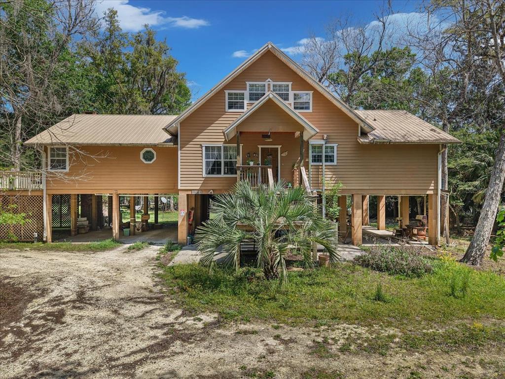 A two-story house with tan siding, a metal roof, and an elevated deck on stilts — 124 NE 824TH STREET, OLD TOWN, FL