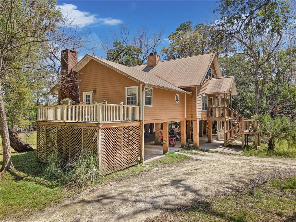 A stilt house with tan siding and a metal roof stands above a gravel driveway — 124 NE 824TH STREET, OLD TOWN, FL