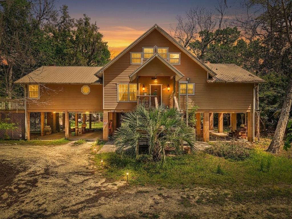 A two-story stilt house with tan siding and a metal roof sits in a wooded area — 124 NE 824TH STREET, OLD TOWN, FL