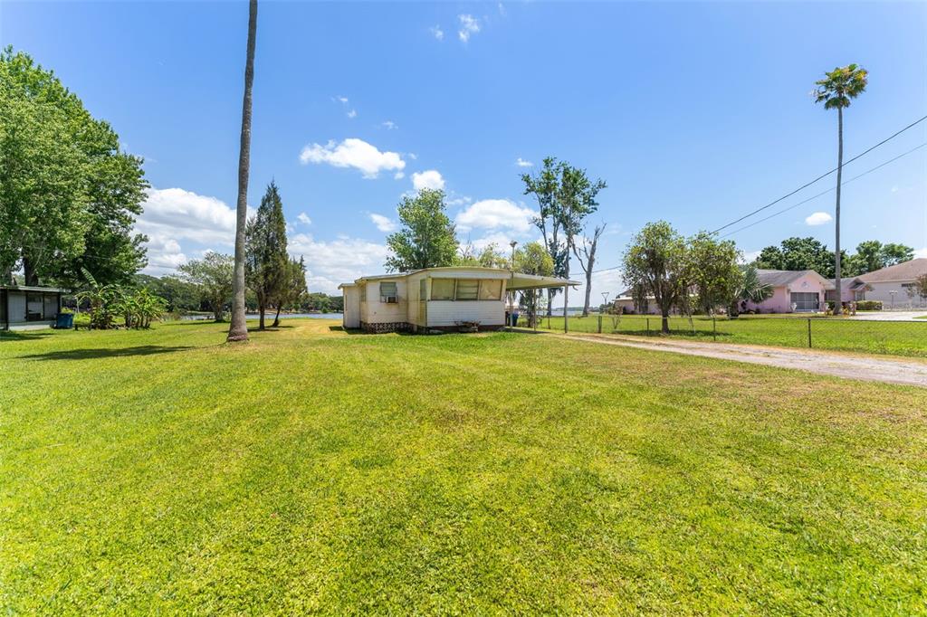 A single-story mobile home sits on a large grassy lot near a body of water — 7558 BERKLEY ROAD, POLK CITY, FL